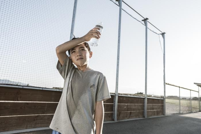A boy tired out after practice wipes his sweaty head (s. asthma, extreme heat, climate)