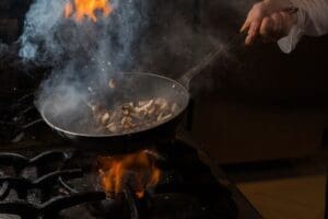 Home Image: Side view mushroom frying with smoke and fire and human hand and pan in stove