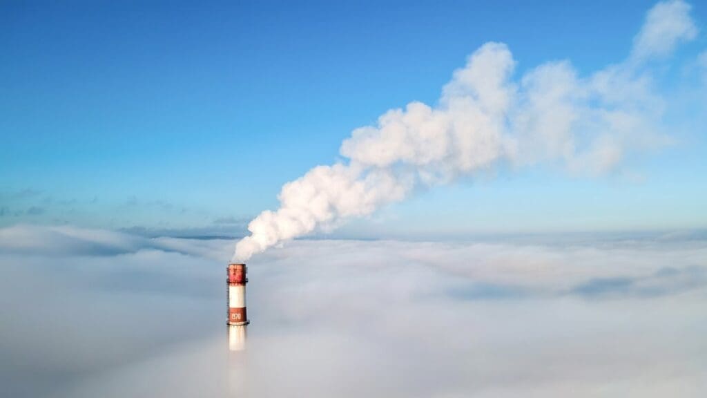 Image: Aerial drone view of thermal station's tube visible above the clouds with smoke coming out