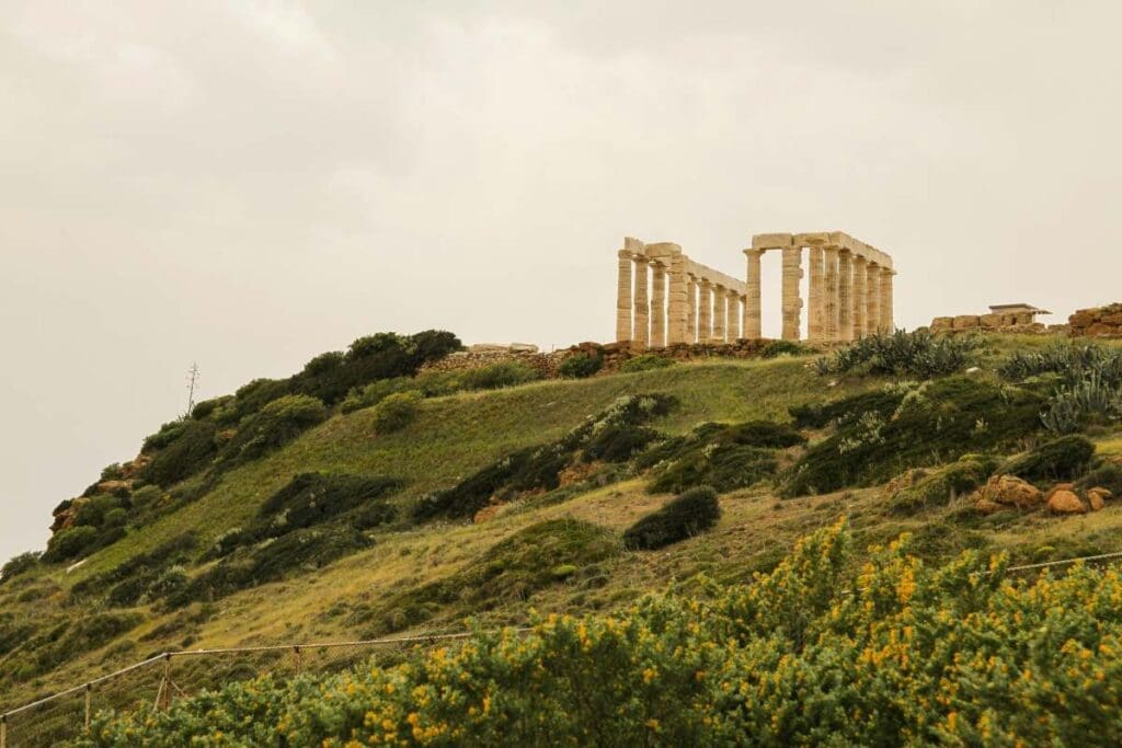 Image: large stone structure sitting on top of a lush green hillside -Sounion, Greece