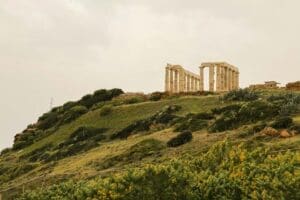 Home Image: large stone structure sitting on top of a lush green hillside -Sounion, Greece