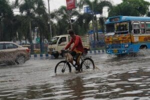 Home Image: a man riding a bike through a flooded street (s. India, monsoon)