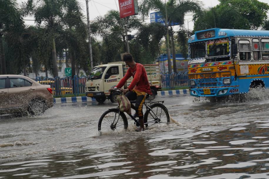 Image: a man riding a bike through a flooded street (s. India, monsoon)