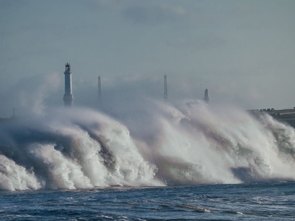 Image: Powerful ocean waves crash dramatically near a lighthouse on the coastline