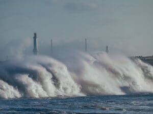 Home Image: Powerful ocean waves crash dramatically near a lighthouse on the coastline