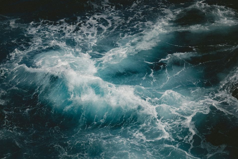 Home Image: turbulent blue ocean wave with white sea foam swirling in dark water
