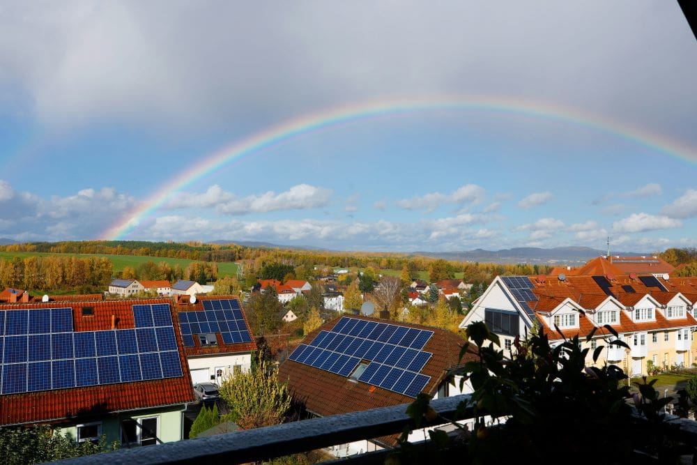 Home Image: A view over a few houses with solar panels and a rainbow in the sky